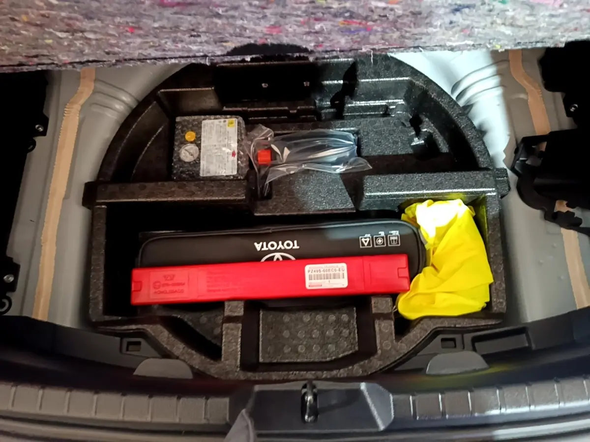 Vue plongeante sur le coffre ouvert d'une Toyota Yaris blanche, montrant le rangement d'accessoires et kit de sécurité.