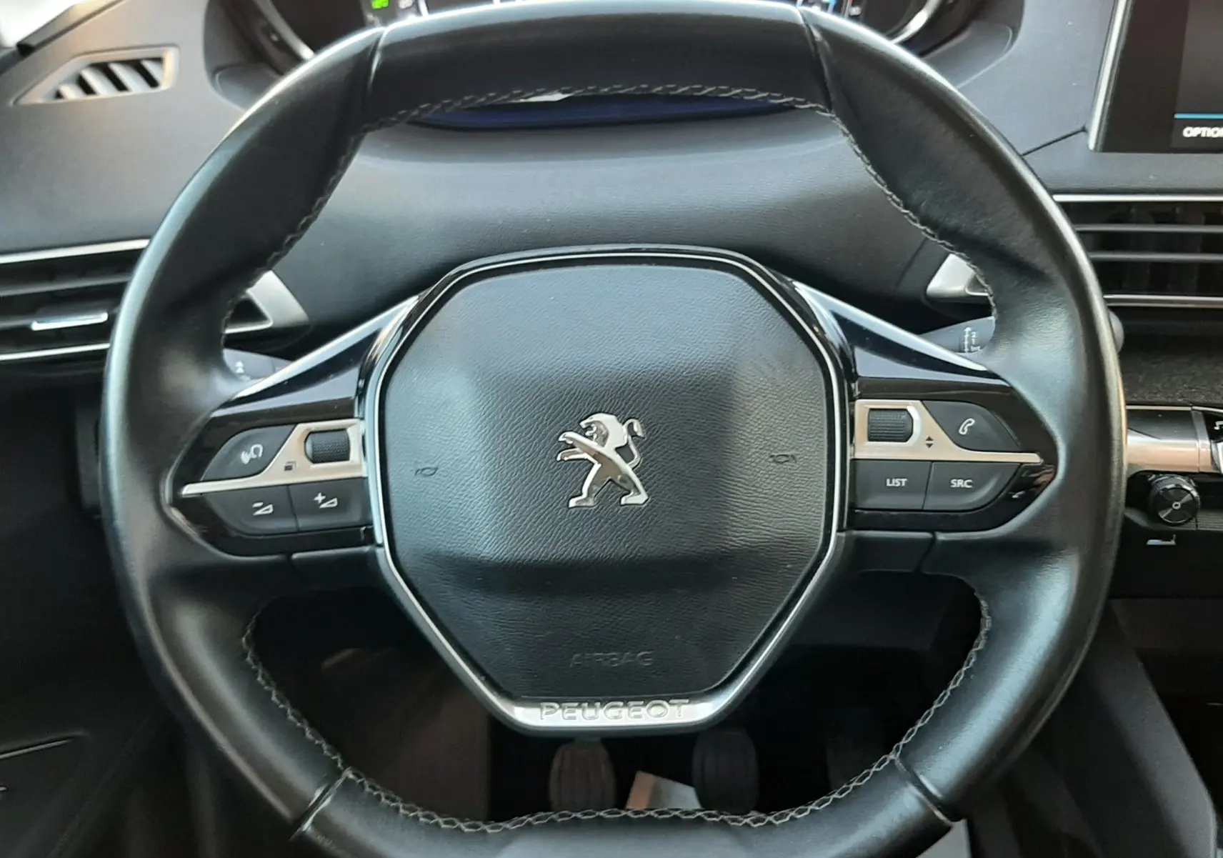 Vue rapprochée du volant noir en cuir du Peugeot 3008 2019, avec commandes intégrées et tableau de bord numérique en arrière-plan.
