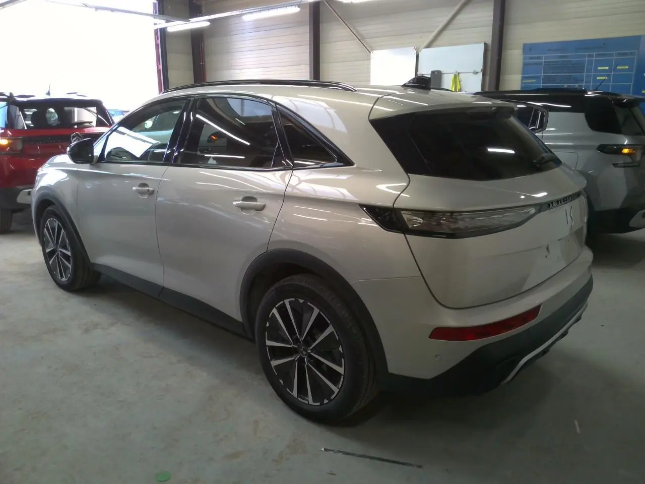 Vue 3/4 arrière droite d'un DS7 Cristal Pearl avec jantes alliage et barres de toit noir brillant en intérieur garage.