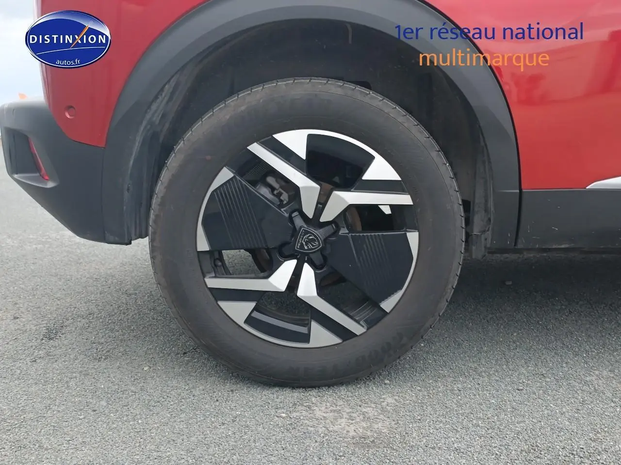 Gros plan sur la roue avant droite avec jante alu noire et argentée du Peugeot 2008 rouge elixir.