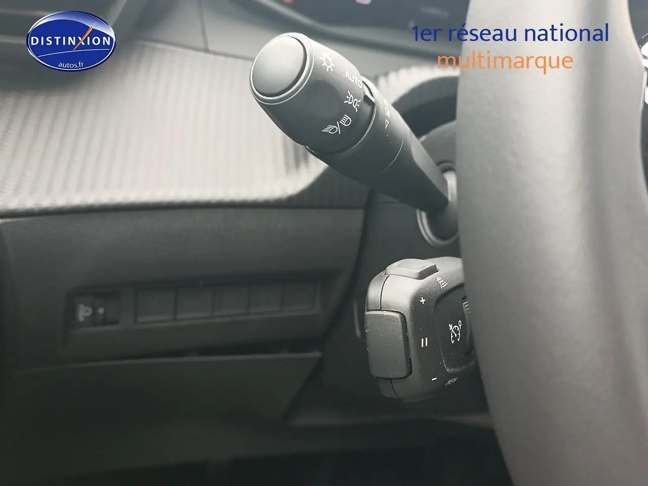 Gros plan sur la commande des phares et régulateur de vitesse derrière le volant d’un Peugeot 2008 rouge elixir.