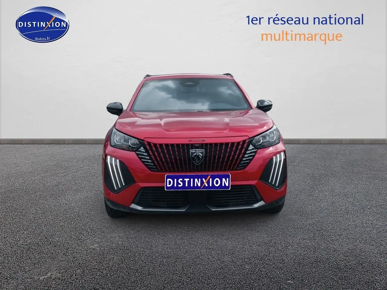 Vue frontale d'un Peugeot 2008 rouge elixir avec calandre noire et feux LED verticaux allumés.