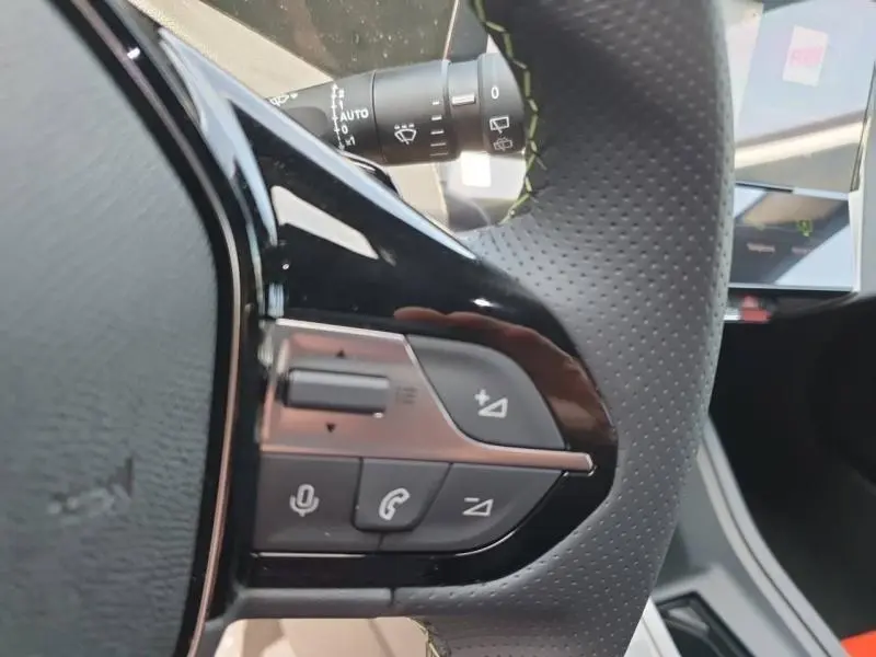 Gros plan sur les commandes multifonctions noires du volant perforé côté gauche du Peugeot 308 blanc Okénite 2026.
