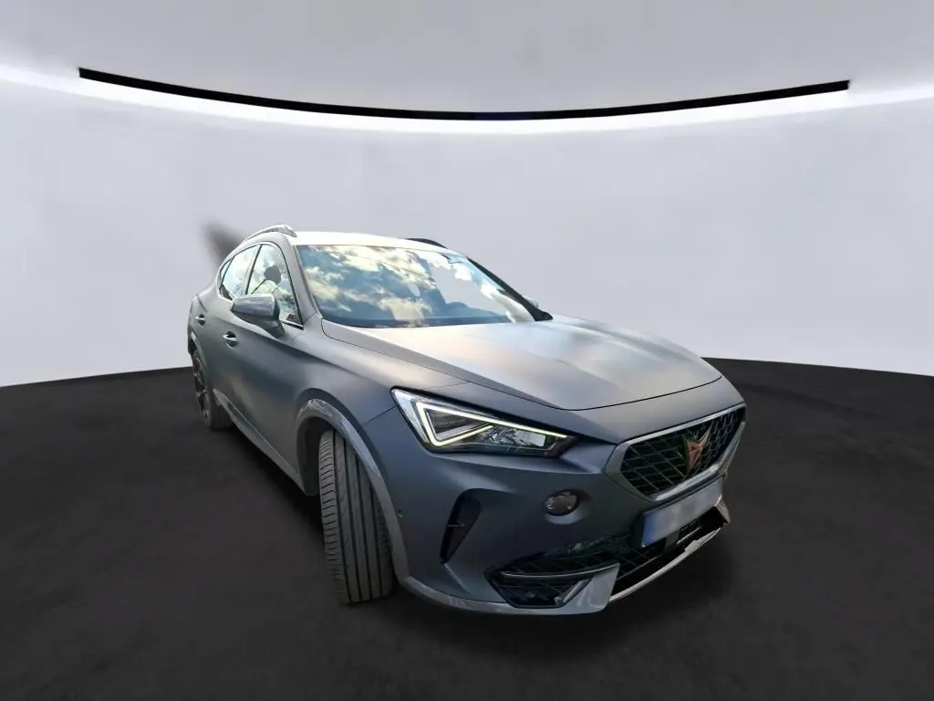 Vue 3/4 avant gauche d'une CUPRA Formentor 1.4 E-HYBRID 2024 en gris foncé mat avec phares LED distinctifs.