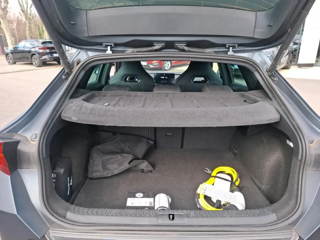 Coffre ouvert d’une CUPRA Formentor gris foncé mat, vue arrière montrant l’espace de chargement avec câble de recharge jaune.