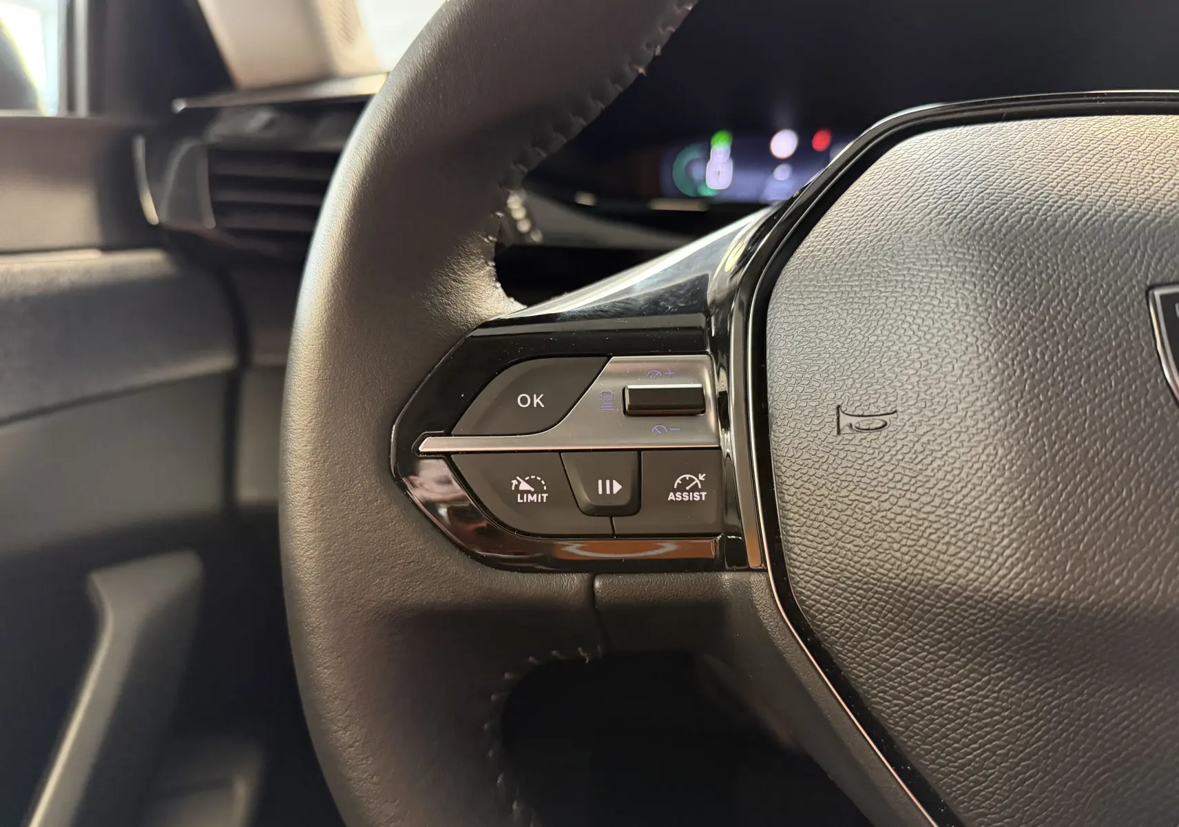 Gros plan sur la partie gauche du volant noir de la Peugeot 308 Hybrid 145, avec commandes de limitation et assistance.