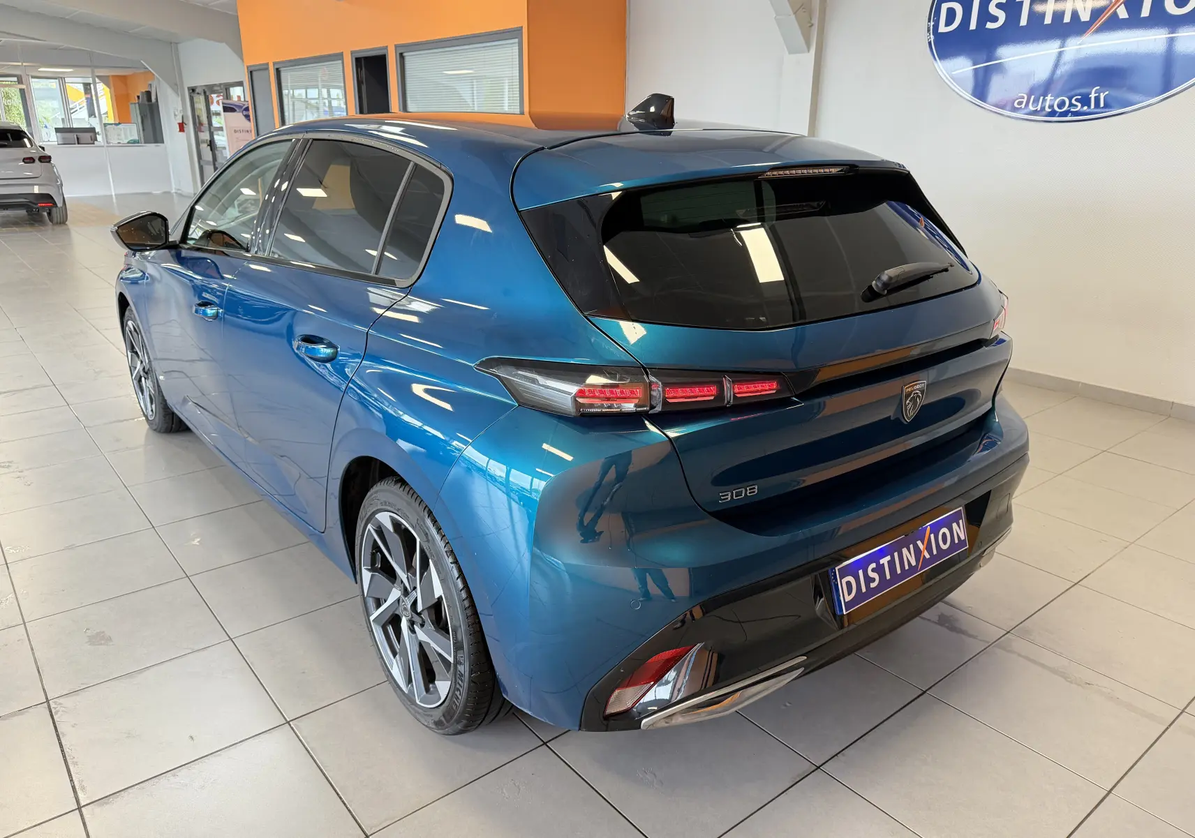 Vue 3/4 arrière droite d'une Peugeot 308 Hybrid 145 bleu obsession avec jantes alliage 17 pouces et vitres surteintées en showroom.