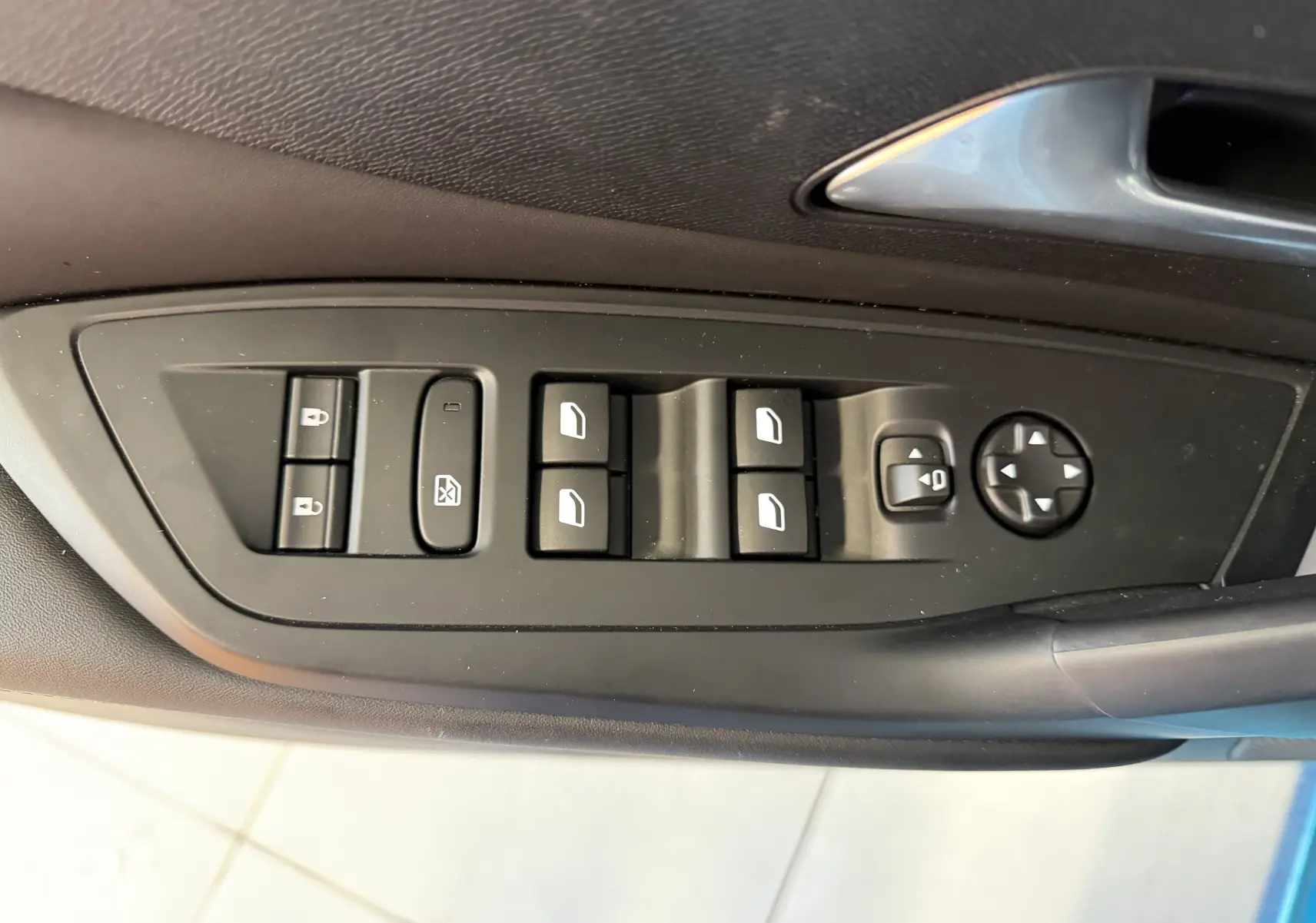 Gros plan sur les commandes de lève-vitres et rétroviseurs sur la porte côté gauche d’une Peugeot 308 Bleu Obsession.