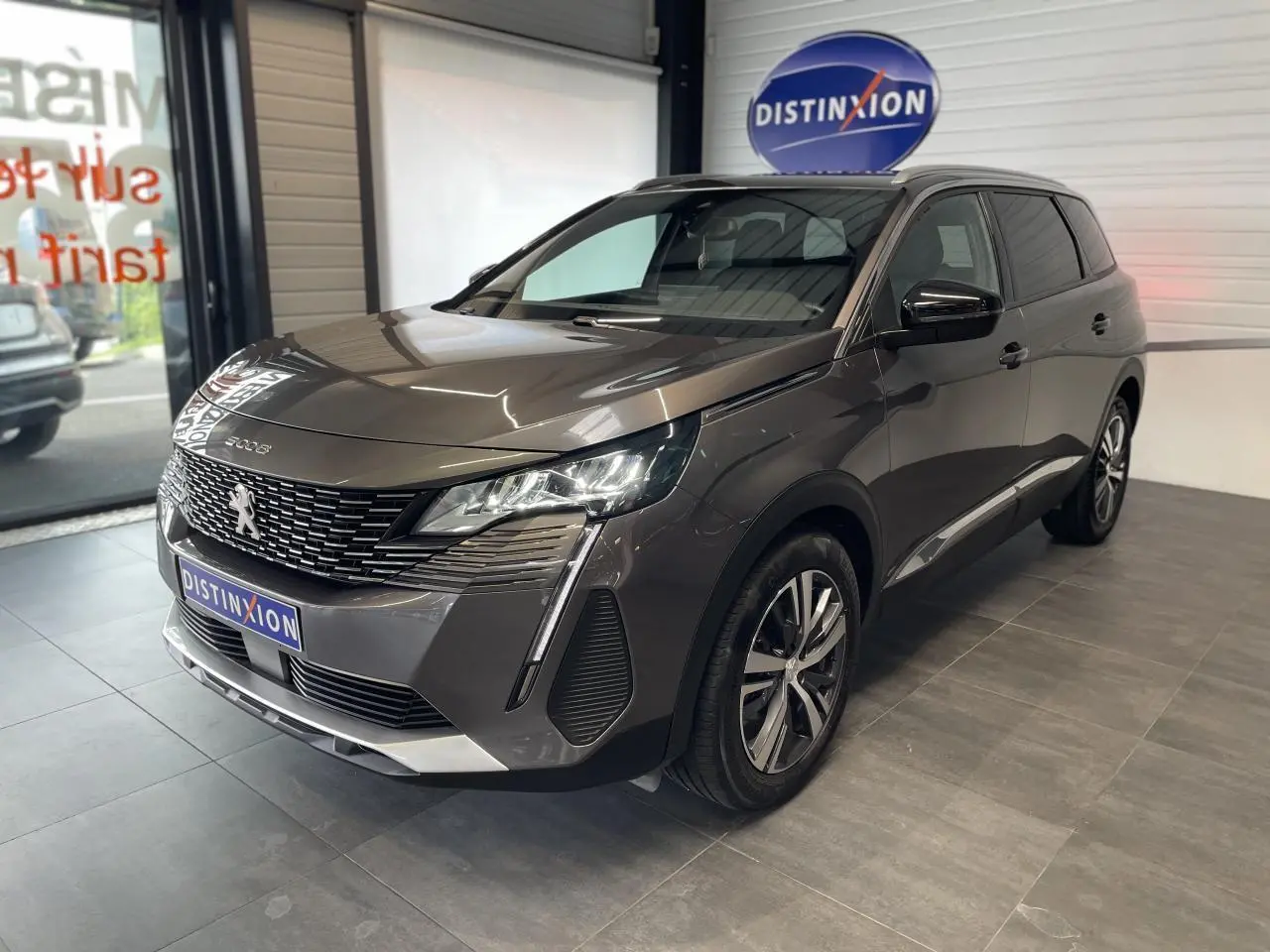 Peugeot 5008 gris platinium vue 3/4 avant droit en intérieur avec calandre chromée et jantes bi-ton 18 pouces.