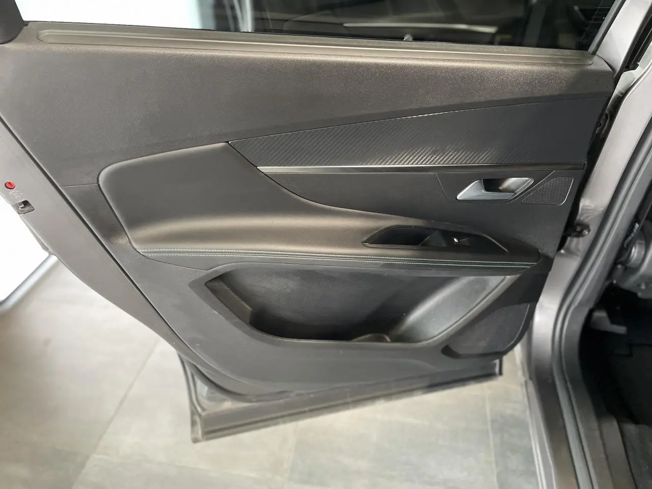 Porte arrière gauche ouverte du Peugeot 5008 gris platinium, avec garniture noire et insert effet carbone.