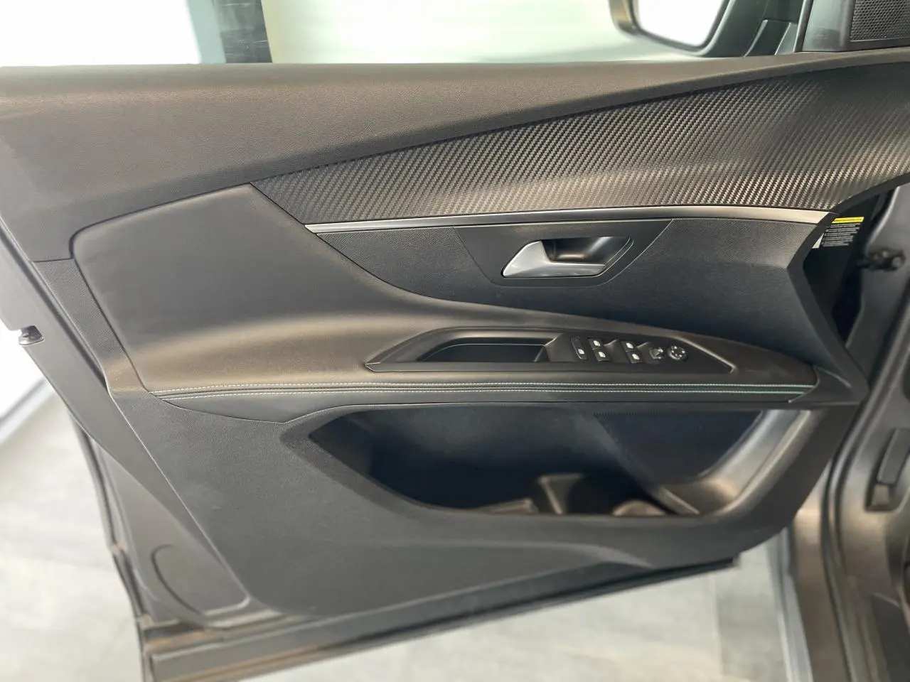 Panneau de porte avant gauche noir avec insert carbone et commandes électriques sur Peugeot 5008 gris platinium 2024