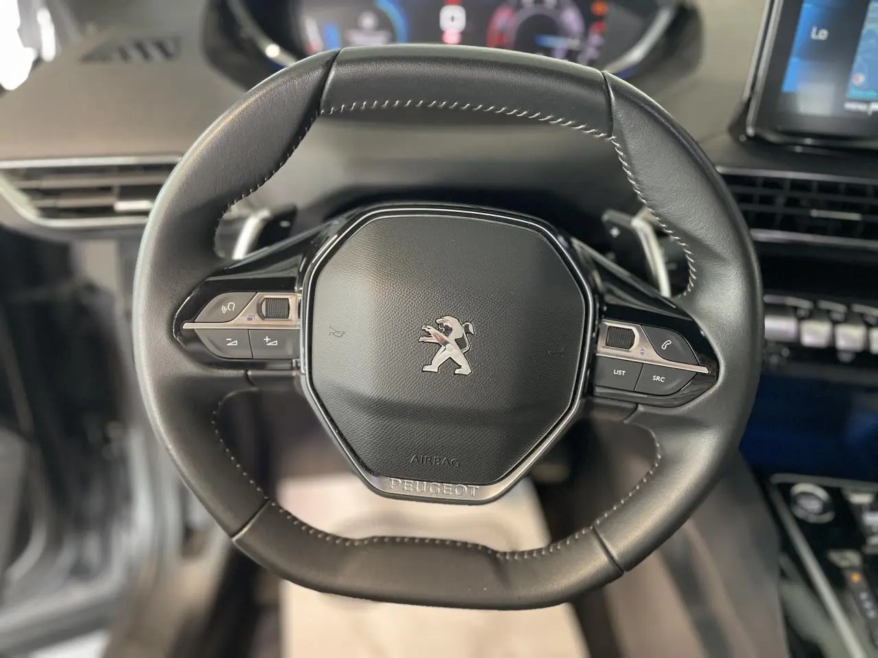 Volant compact en cuir noir du Peugeot 5008 2024 avec commandes intégrées et logo lion central visible.