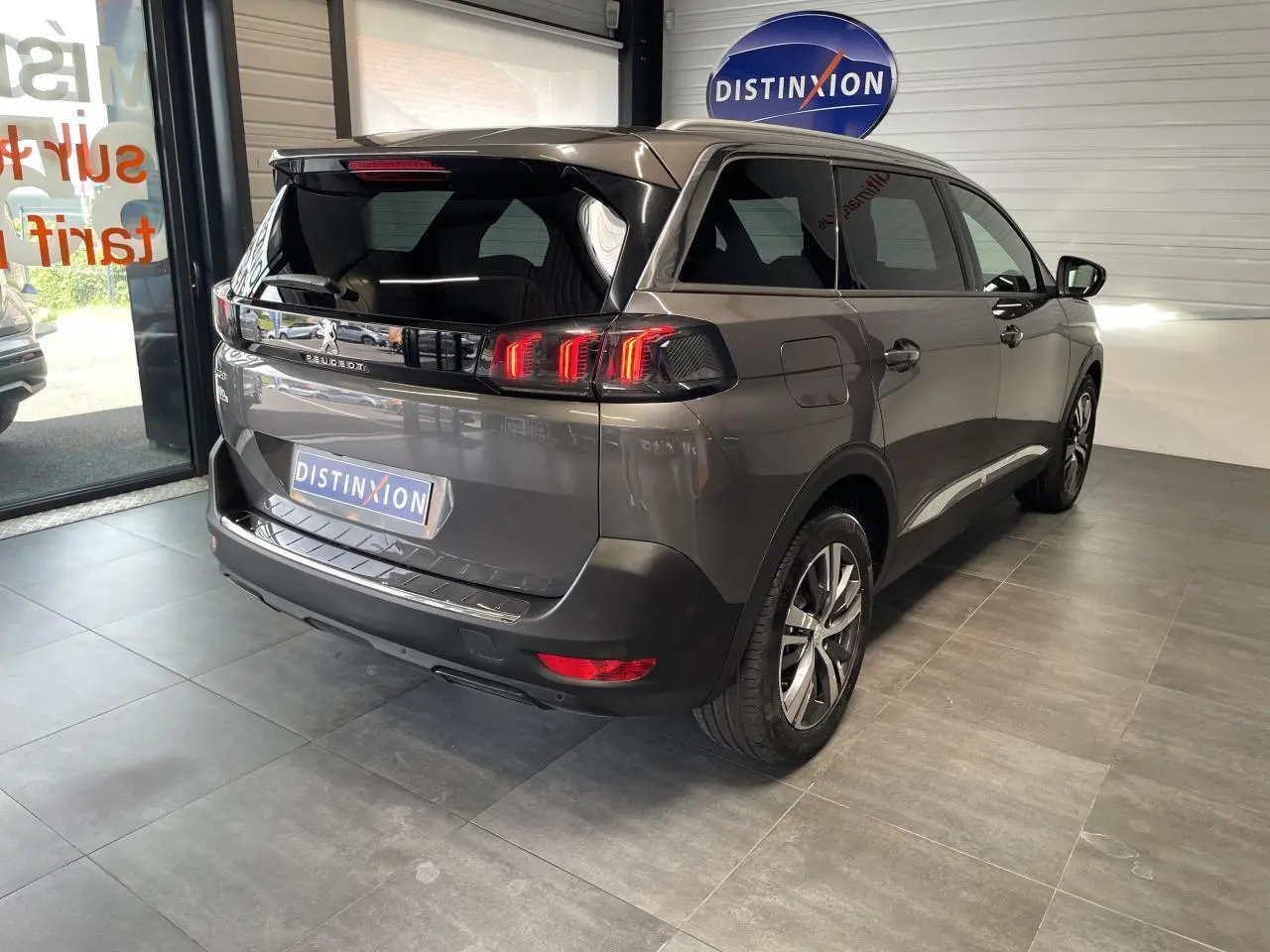 Vue 3/4 arrière droit du Peugeot 5008 gris platinium avec feux LED 3D et vitres arrière surteintées en showroom.