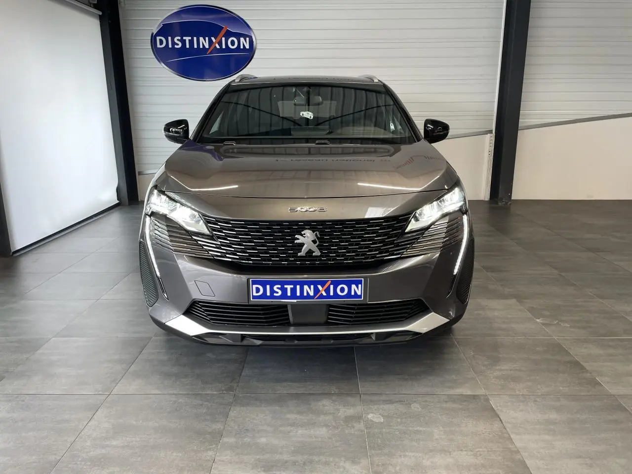 Vue frontale d'un Peugeot 5008 gris platinium avec calandre à damier chromé et feux LED allumés en showroom.