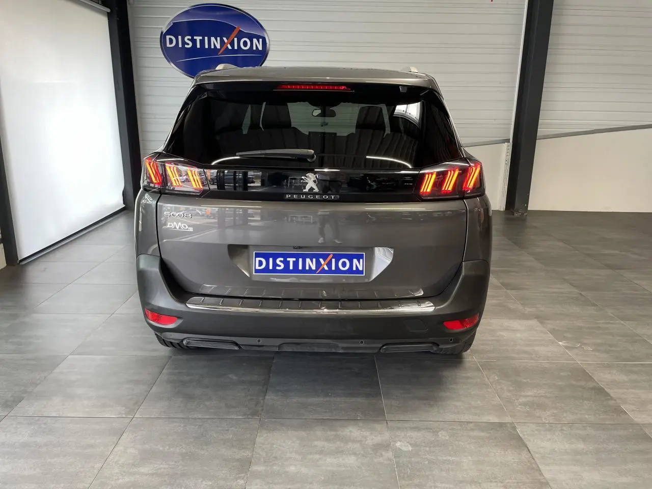 Vue arrière du Peugeot 5008 gris platinium 2024 avec feux LED 3D et logo Peugeot visible en intérieur showroom.