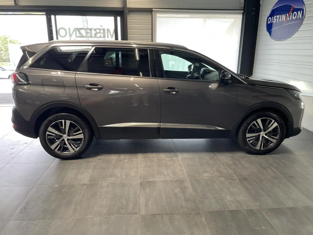 Profil droit du Peugeot 5008 gris platinium 2024 avec jantes alliage bi-ton et vitres arrière surteintées.