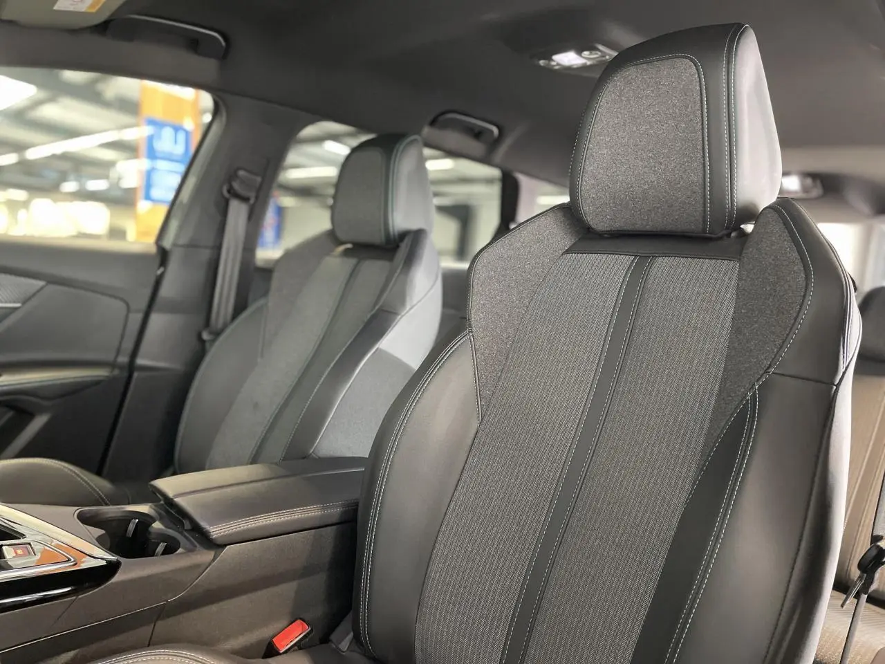Gros plan sur les sièges avant gris TEP et tissu du Peugeot 5008 2024 avec accoudoir central et coutures contrastées.