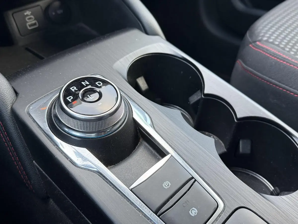 Gros plan sur la console centrale du Ford Kuga 2022 ST-Line, avec sélecteur rotatif de boîte auto et surpiqûres rouges sur sellerie noire.