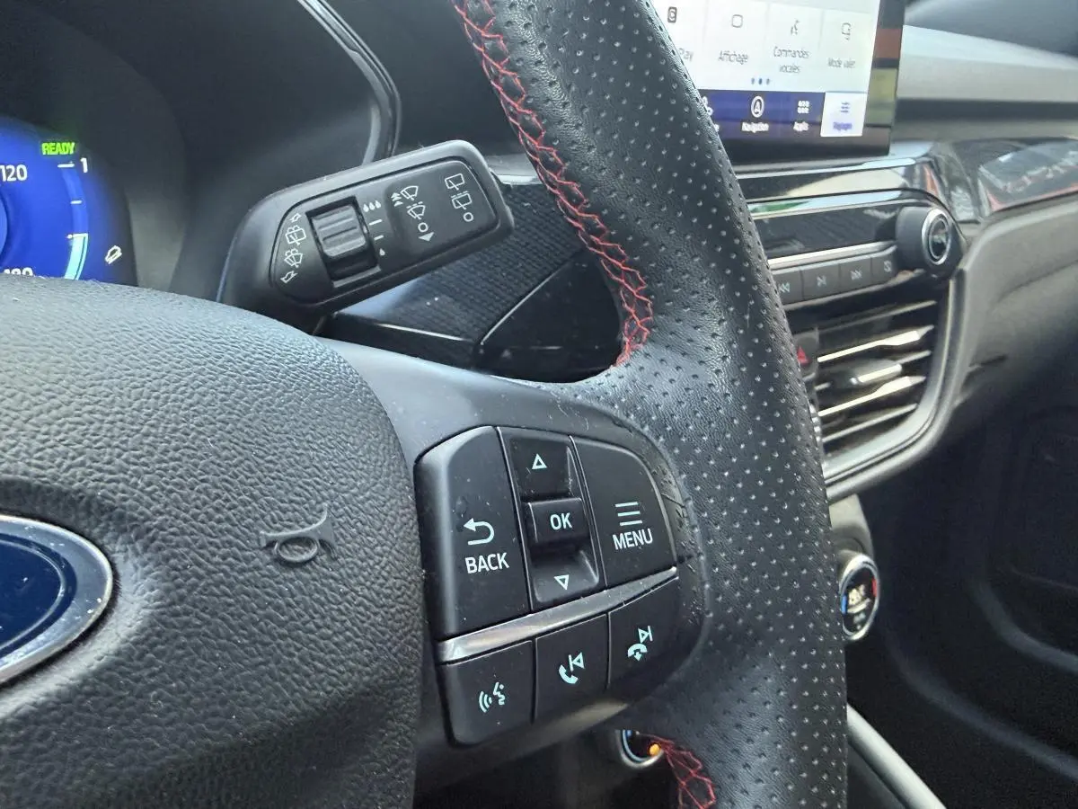 Gros plan sur le volant perforé noir avec surpiqûres rouges du Ford Kuga 2022, tableau de bord et commandes visibles.