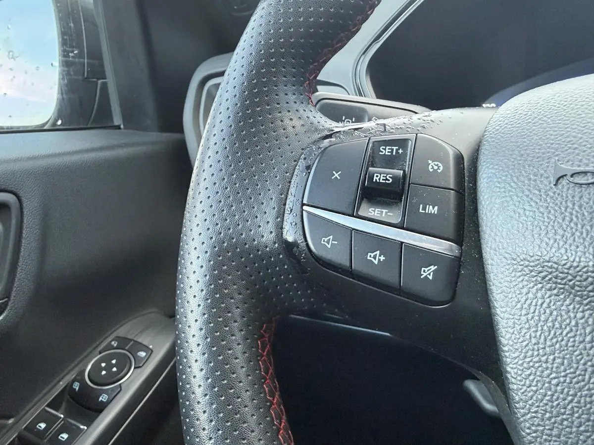 Gros plan sur le volant perforé noir avec surpiqûres rouges du Ford Kuga ST-Line 2022, côté gauche avec commandes intégrées.