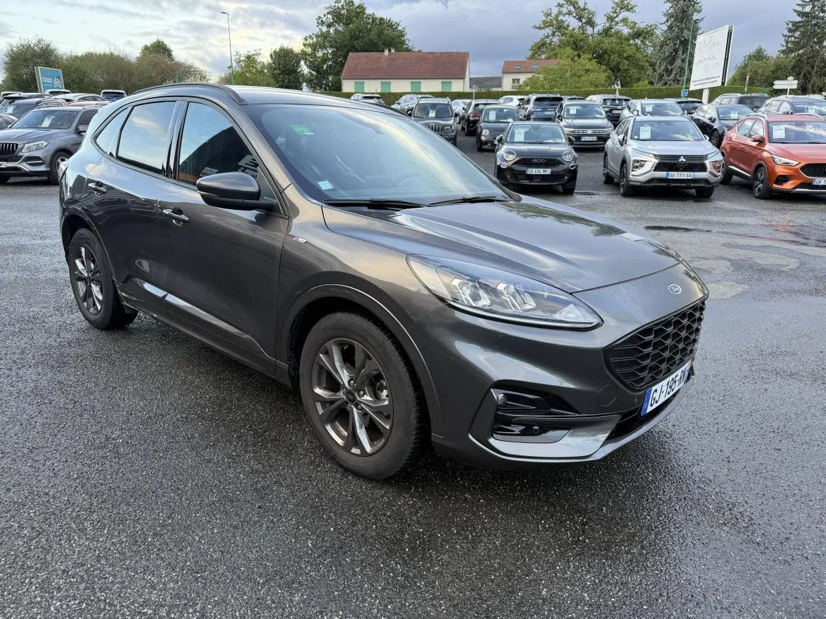 Ford Kuga gris métallisé en vue 3/4 avant droit, avec calandre et jantes alliage 18 pouces ST-Line visibles.
