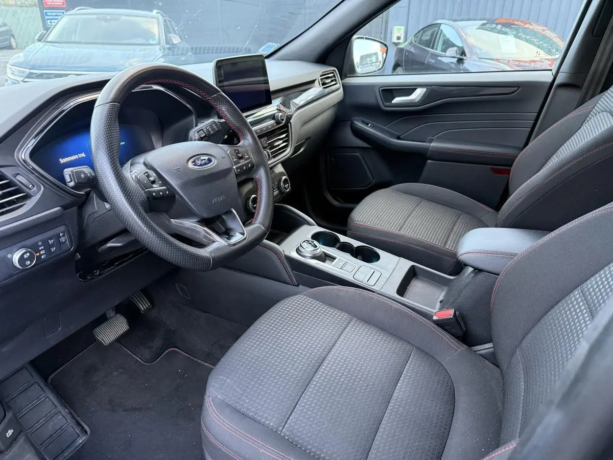 Intérieur avant du Ford Kuga 2022 gris, vue côté conducteur, volant ST-Line avec surpiqûres rouges et console centrale.