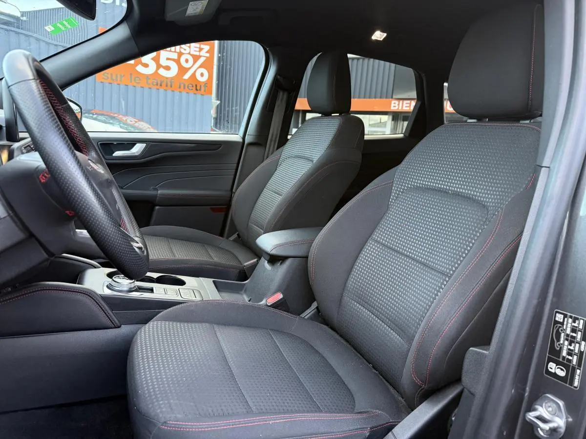 Vue intérieure côté conducteur du Ford Kuga 2022 avec sièges sport tissu noir et surpiqûres rouges ST-Line.
