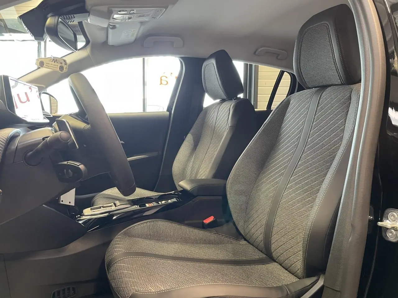 Vue intérieure côté conducteur de la Peugeot 208 noire, mettant en valeur les sièges tissu gris et le volant compact cuir.