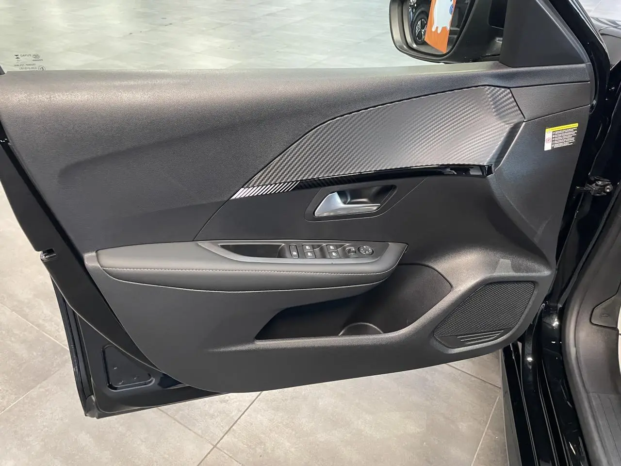 Vue intérieure côté gauche de la porte noire du Peugeot 208 Allure 2025 avec insert effet carbone et commandes électriques.