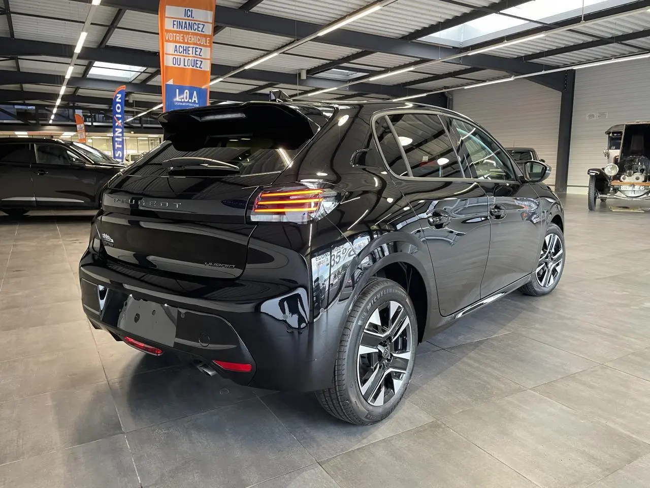 Peugeot 208 hybride noire vue 3/4 arrière droit en intérieur avec jantes alliage bi-tons et feux LED.