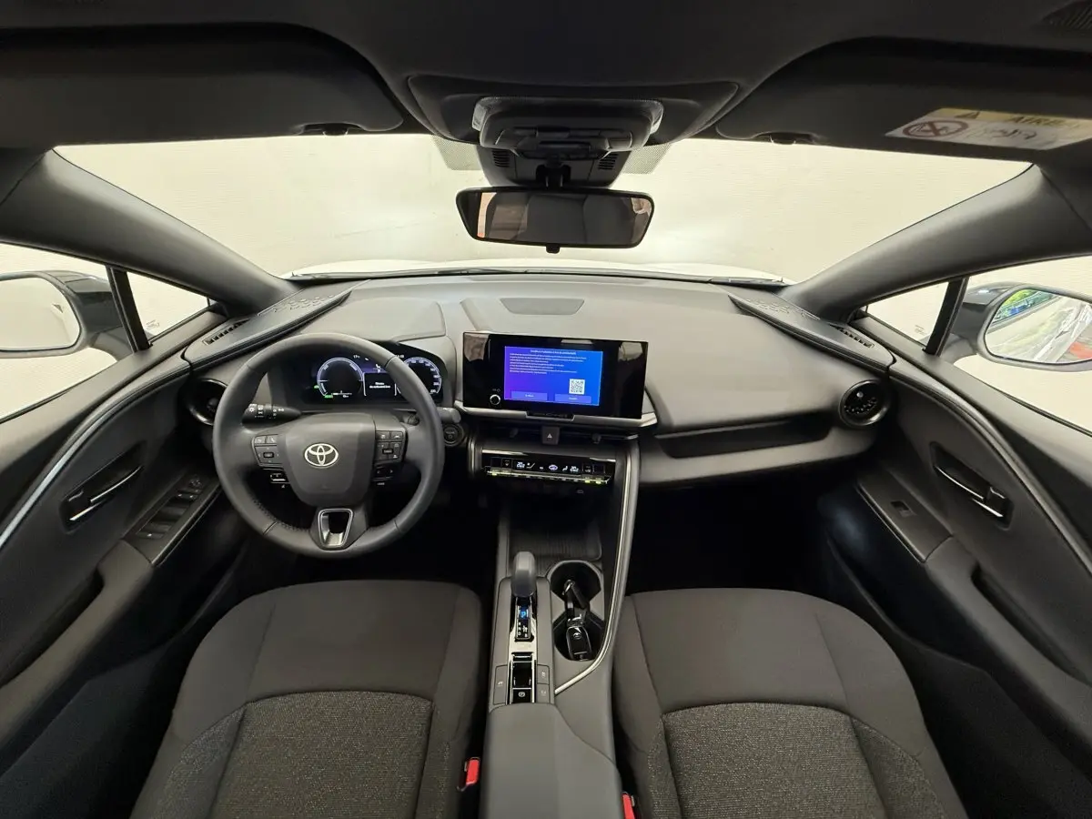 Vue intérieure avant du Toyota C-HR 1.8 Hybride blanc, tableau de bord moderne avec écran tactile central et volant multifonctions.