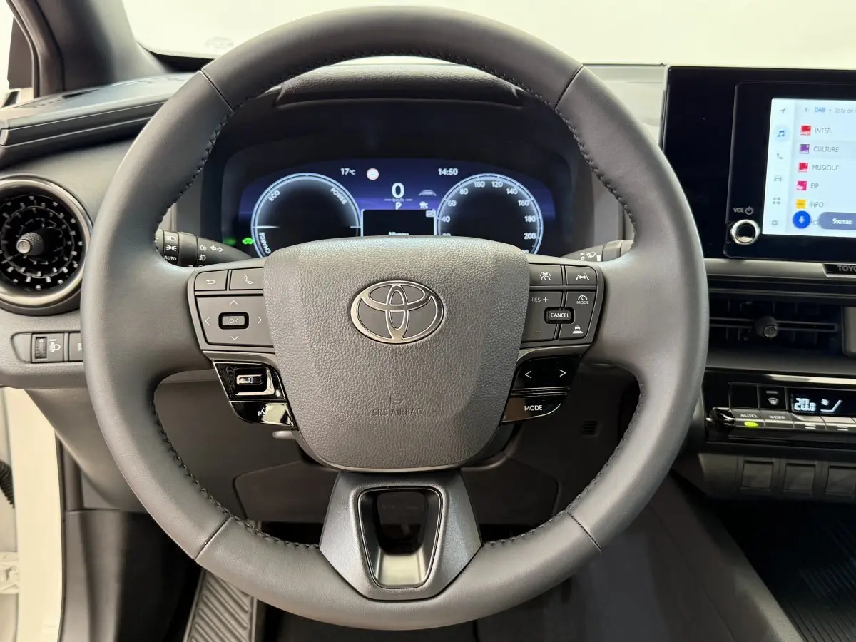 Vue rapprochée du volant cuir noir du Toyota C-HR 1.8 Hybride 2024 avec tableau de bord numérique et écran tactile.