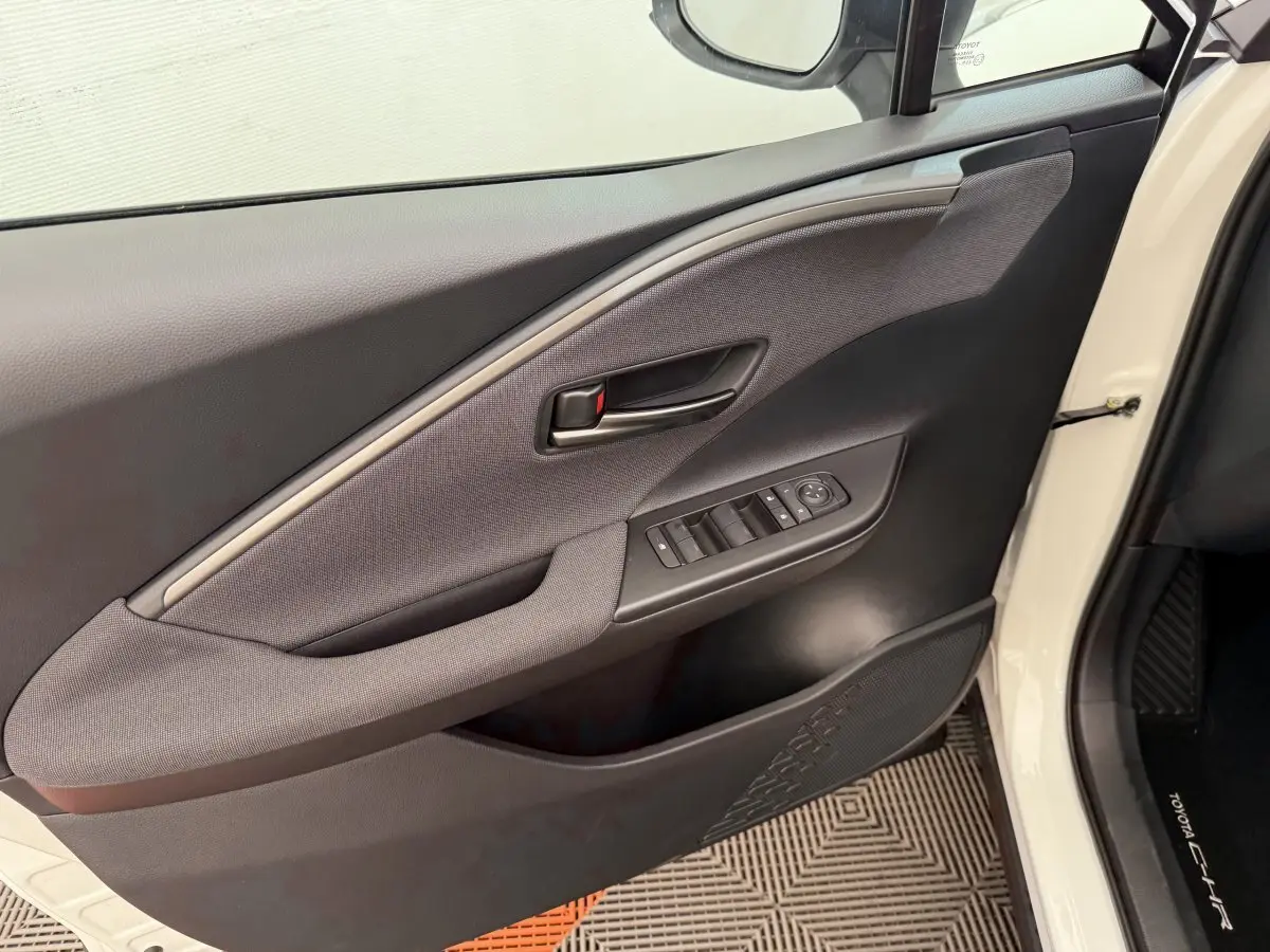 Vue rapprochée de la porte avant gauche blanche du Toyota C-HR 1.8 Hybride 140 Dynamic avec commandes de vitres et poignée noire.