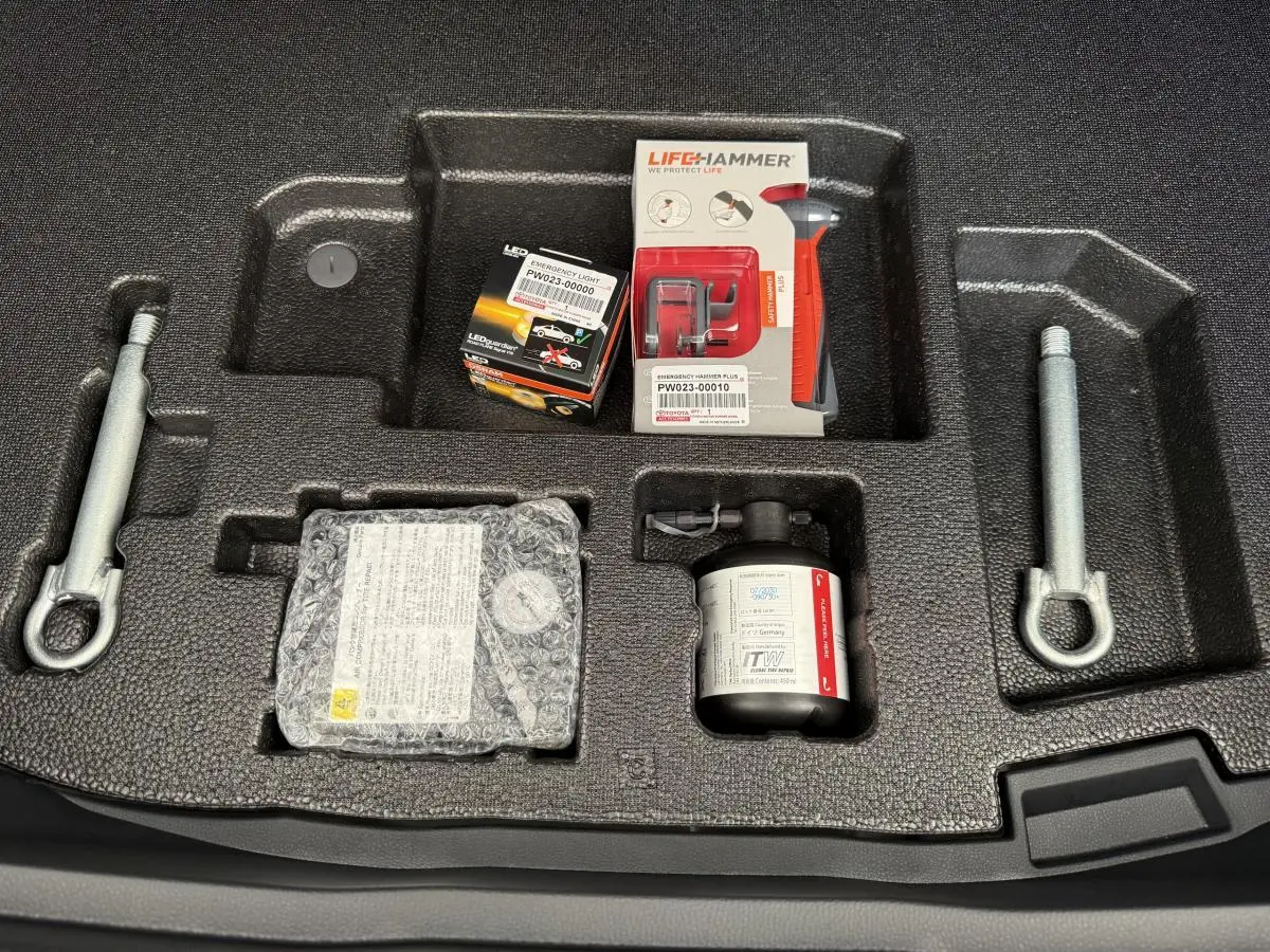 Vue plongeante sur le coffre d’un Toyota C-HR blanc 2024, montrant le rangement avec outils et kit de réparation pneus.