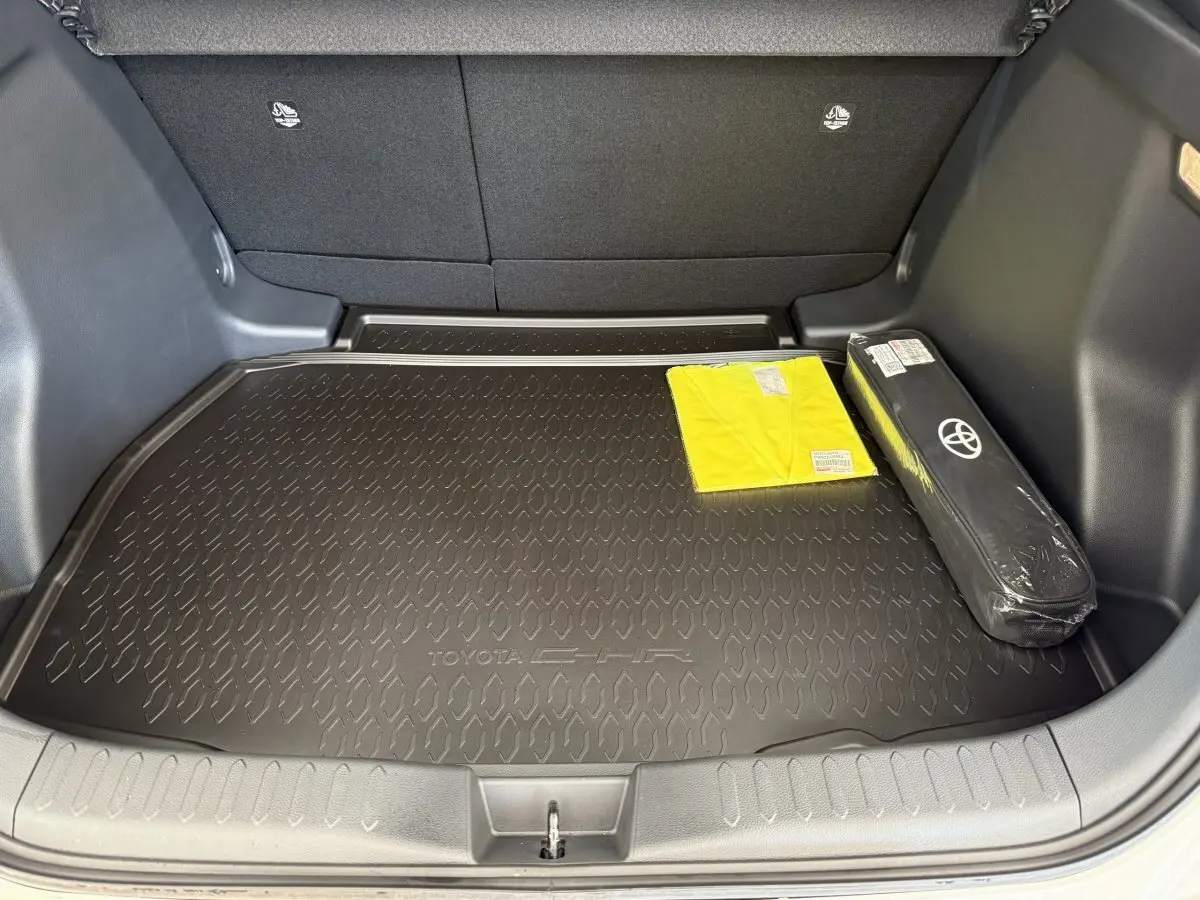 Coffre ouvert du Toyota C-HR blanc 2024, vue arrière, avec tapis de coffre noir marqué C-HR et accessoires rangés.