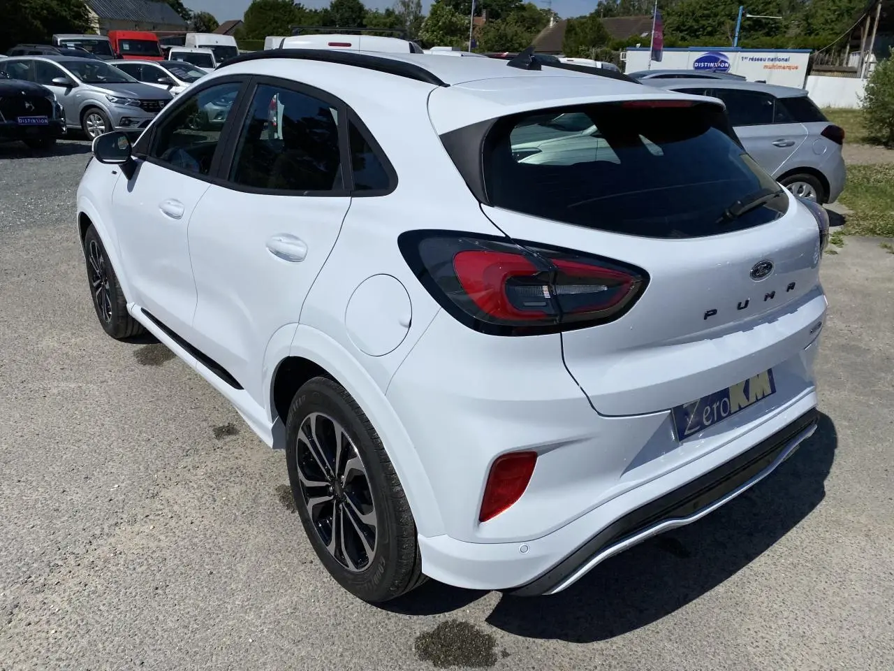 Vue 3/4 arrière droite d'une Ford Puma blanche Glacier avec jantes noires et barres de toit noires.