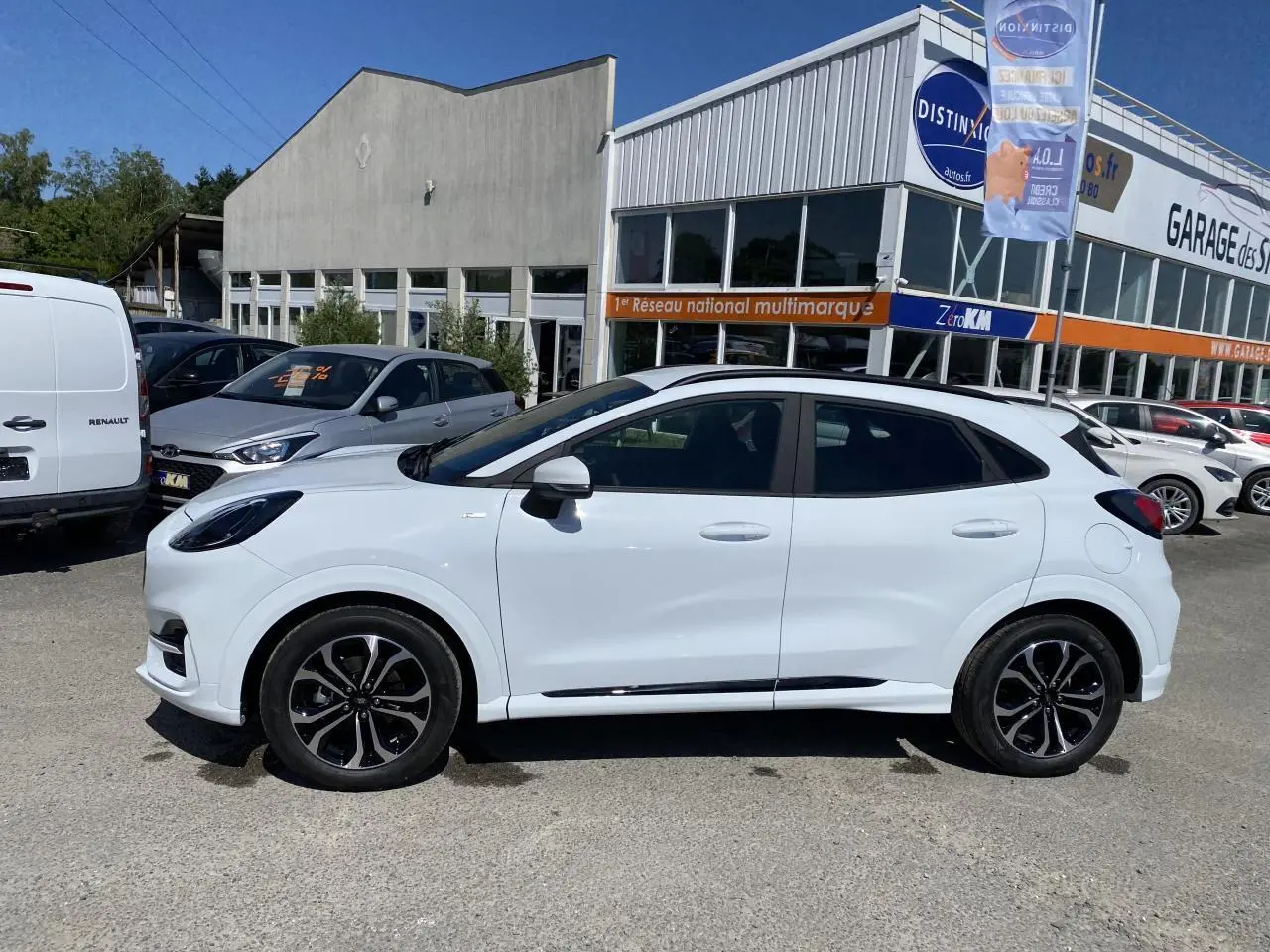 Vue de profil côté gauche d’un Ford Puma blanc Glacier avec jantes alliage noires et barres de toit noires, stationné en extérieur.