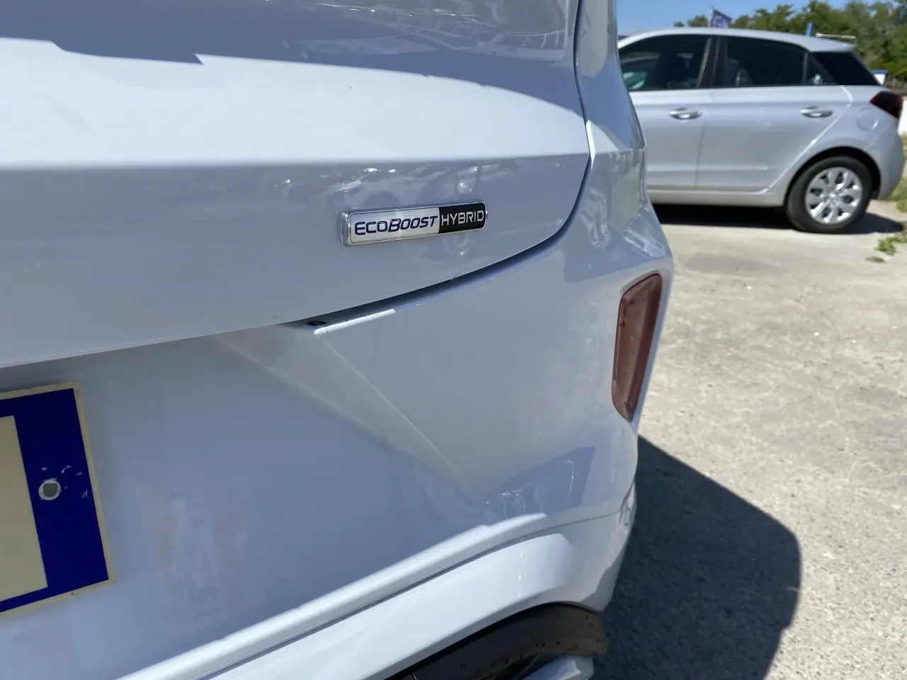 Gros plan sur l'arrière droit blanc glacier d'un Ford Puma avec badge EcoBoost Hybrid visible.