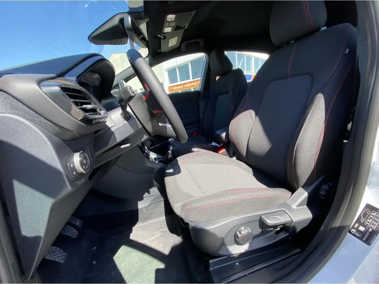 Vue intérieure côté conducteur du Ford Puma blanc glacier 2022, sièges tissu noir avec surpiqûres rouges et volant sport.