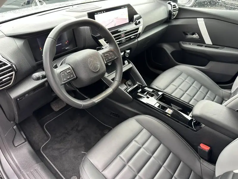 Vue intérieure côté conducteur du Citroën C4 X 2025 gris Mercury, avec tableau de bord numérique et sièges cuir noirs.
