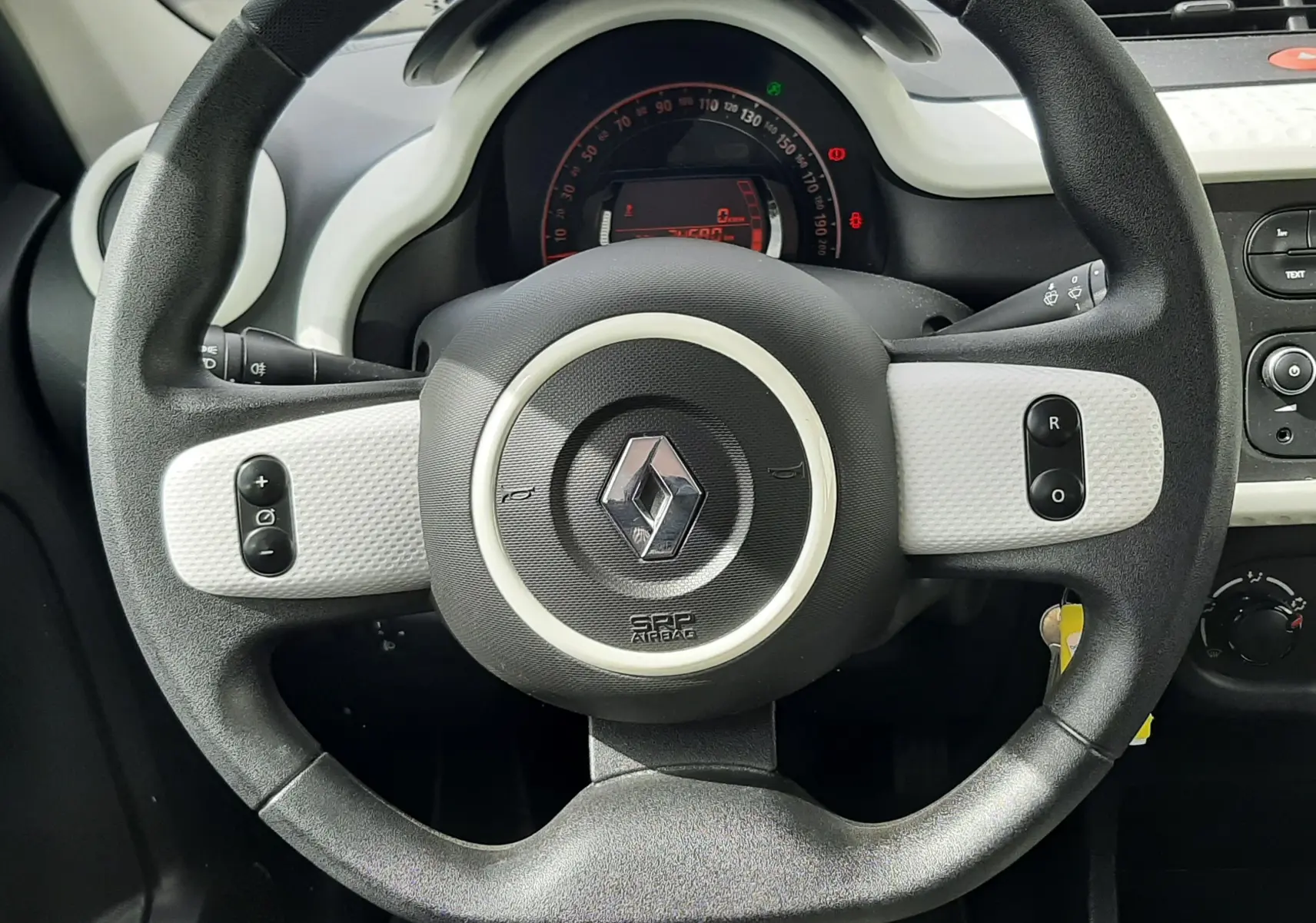 Vue intérieure du tableau de bord et volant de la Renault Twingo III blanche, avec levier de vitesse manuel et commandes centrales visibles.