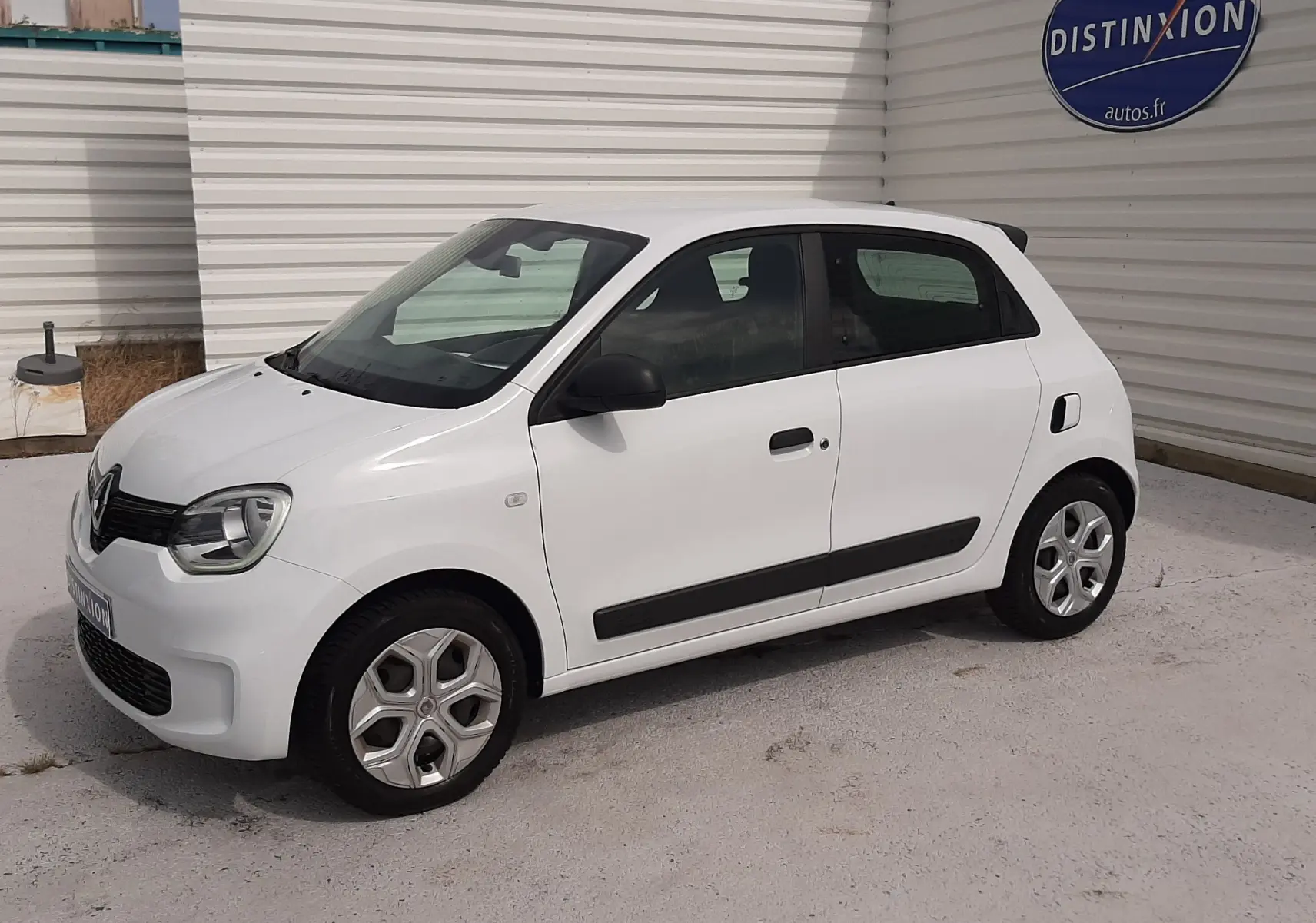 Vue de face d'une Renault Twingo III blanc cristal avec calandre noire et phares allumés sur fond clair.