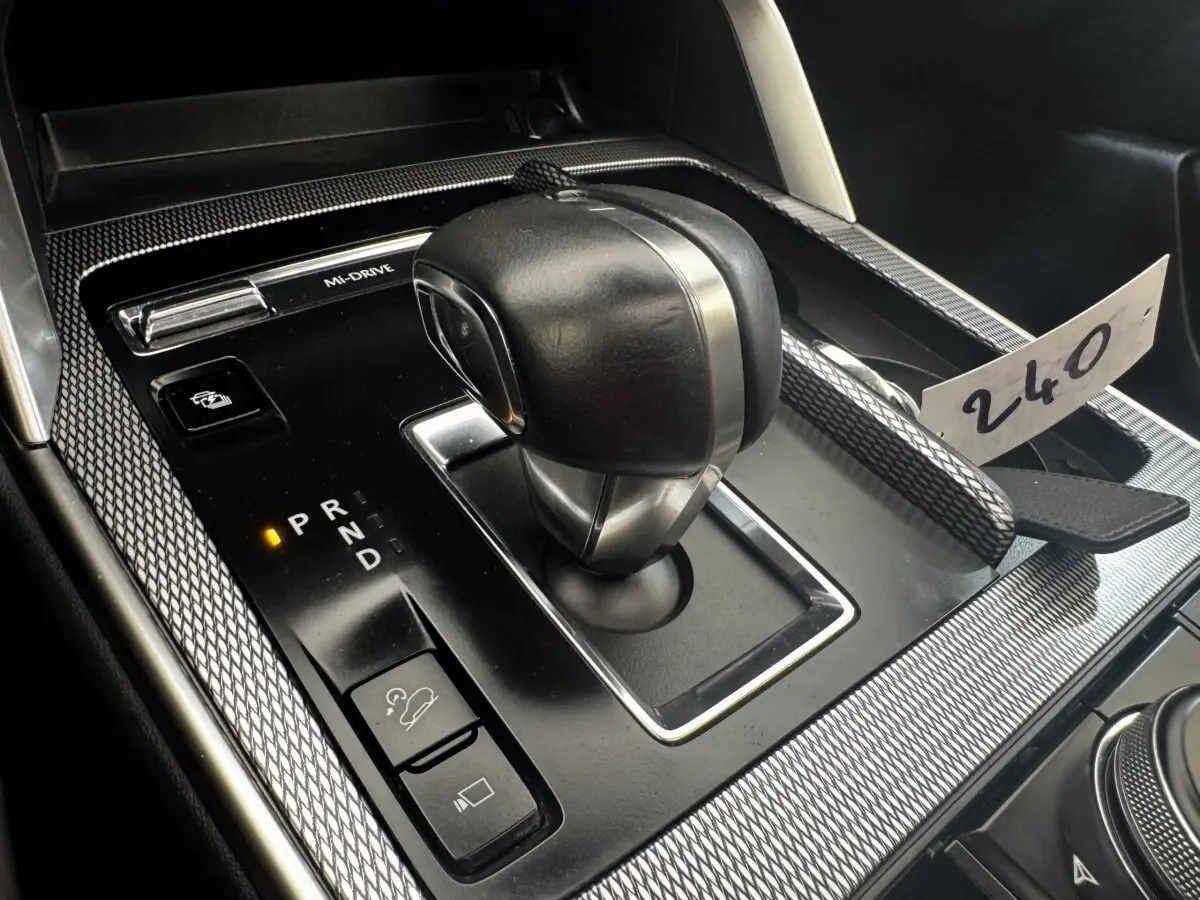Gros plan sur la console centrale noire du Mazda CX-60 2024, avec levier de vitesse automatique et molette de sélection.