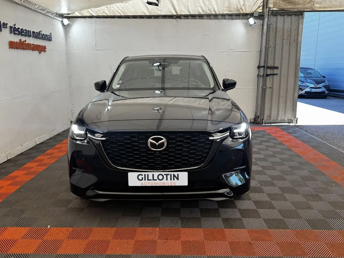 Vue frontale du Mazda CX-60 noir 2024 avec calandre imposante et phares LED allumés dans un showroom.