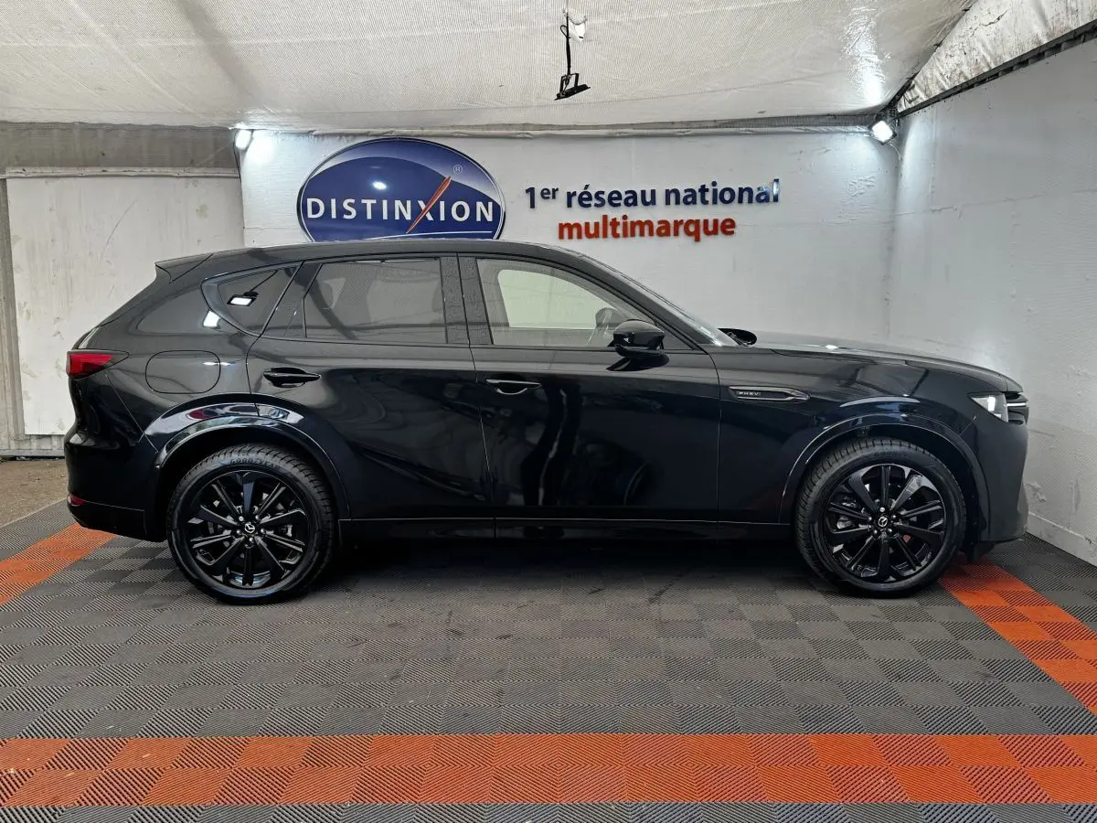 Vue de profil côté gauche du SUV Mazda CX-60 noir brillant avec jantes noires dans un garage éclairé.