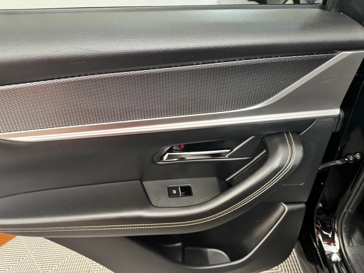 Vue intérieure côté gauche de la porte avant noire du Mazda CX-60 avec poignée chromée et surpiqûres beiges.