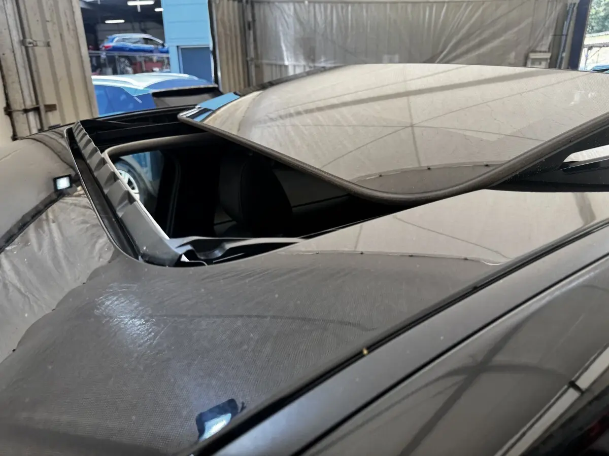 Toit ouvrant panoramique ouvert sur le côté gauche d'un Mazda CX-60 noir, vue rapprochée en intérieur d'atelier.