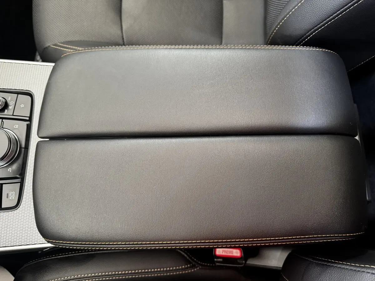 Vue rapprochée de l'accoudoir central en cuir noir avec surpiqûres beiges du Mazda CX-60 2024.