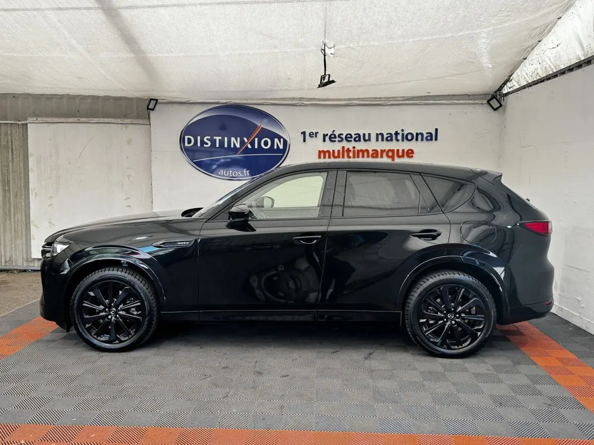 Vue latérale droite du Mazda CX-60 noir 2024 avec jantes noires et vitres teintées dans un showroom.