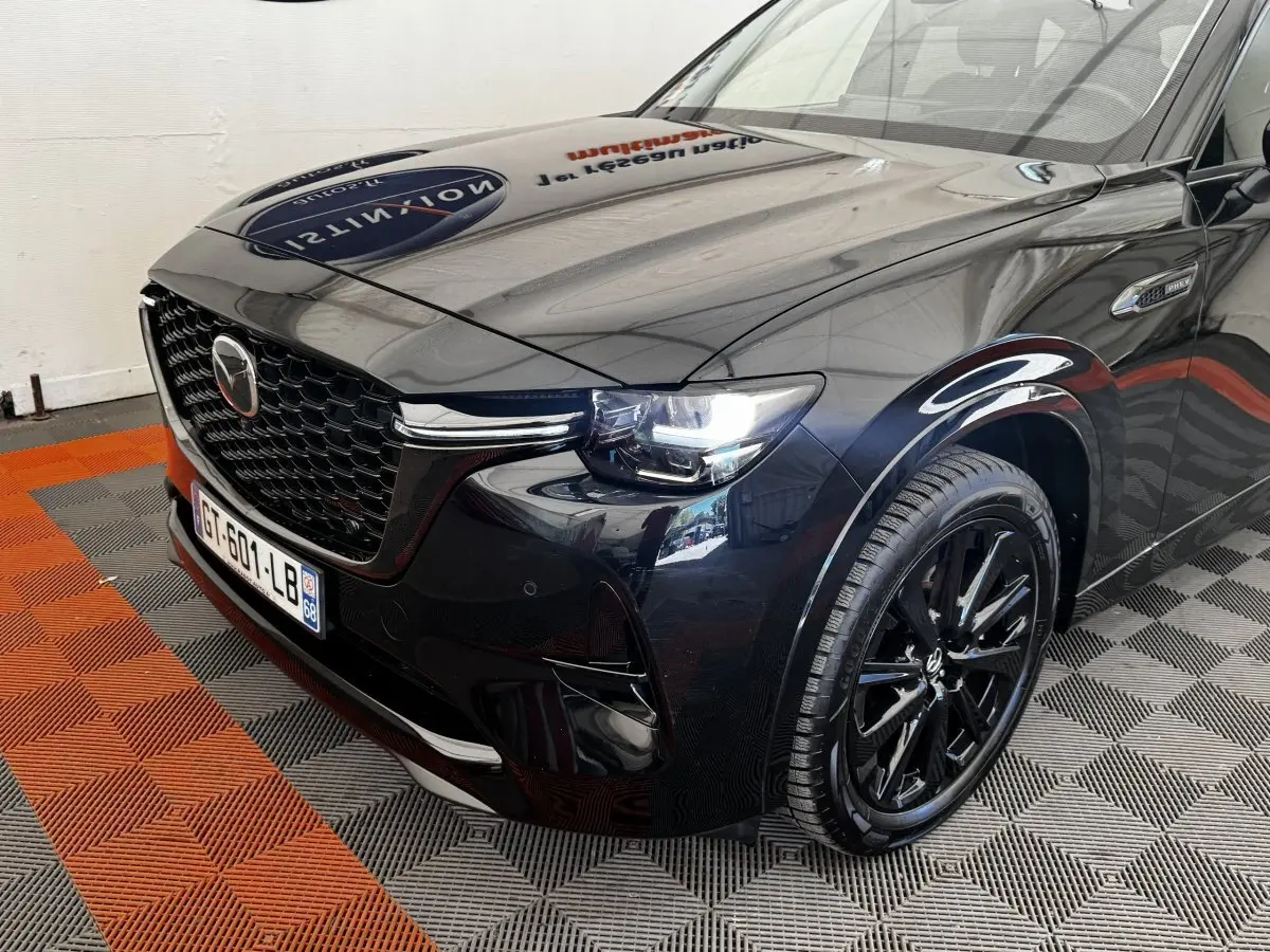 Vue 3/4 avant droit du Mazda CX-60 noir brillant avec calandre imposante et phares LED allumés.
